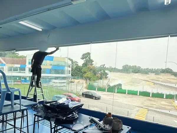 Installer applying silver reflective heat rejection window film to school campus classroom glass